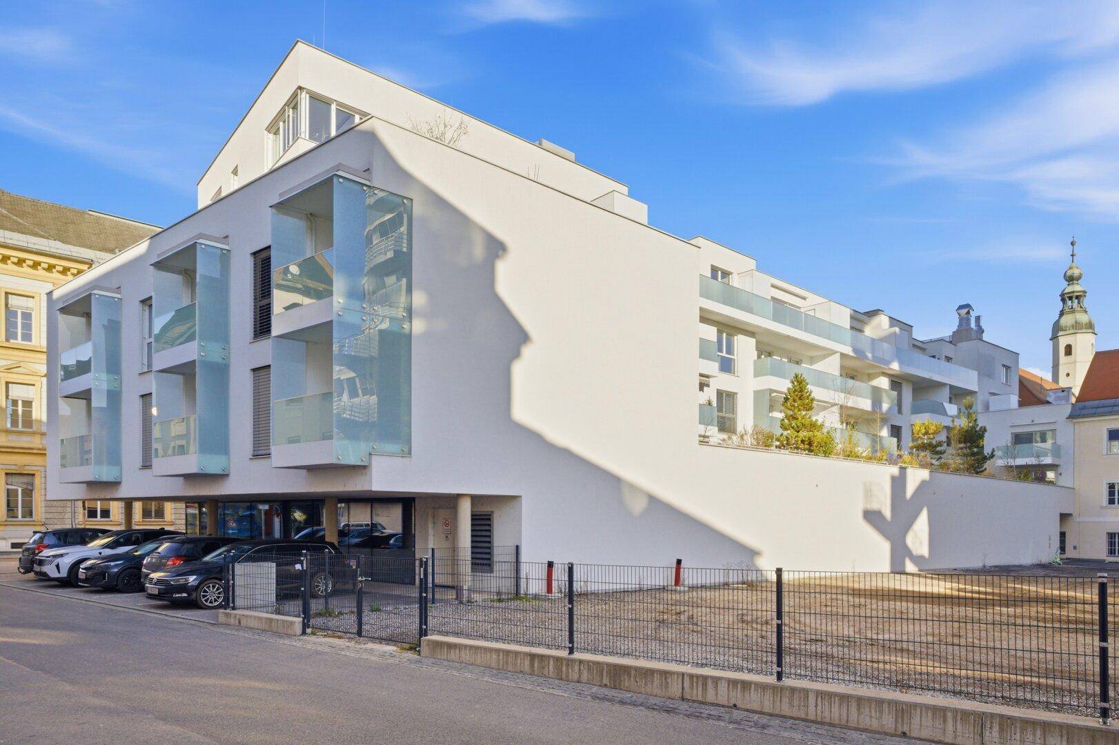 Moderne Wohnanlage mit weißer Fassade, Balkonen und Parkplätzen im Freien.