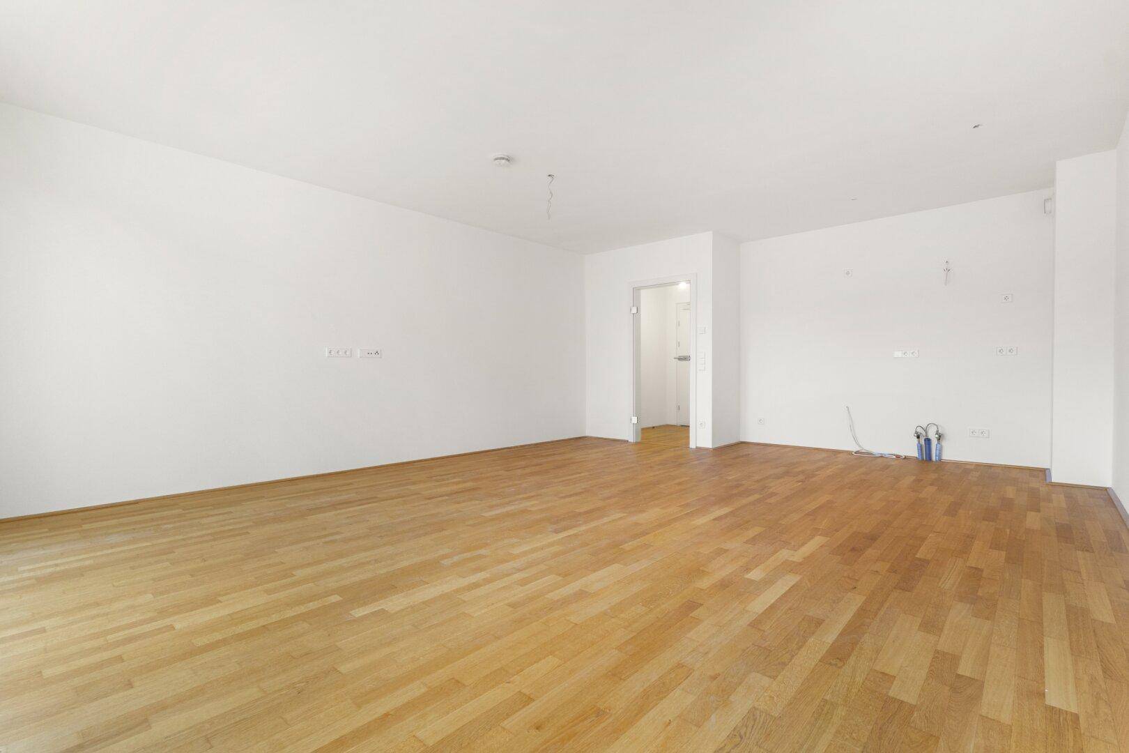 Geräumiger, heller Raum mit Parkettboden und Zugang zu einem weiteren Zimmer.