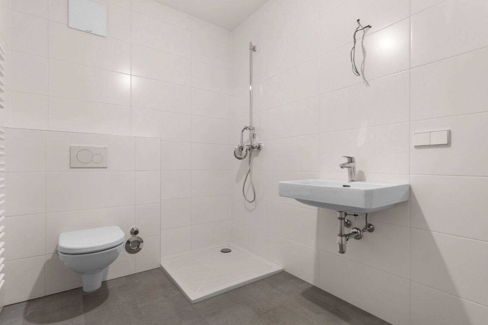 Modernes Badezimmer mit weißen Fliesen, Dusche, WC und Waschbecken.
