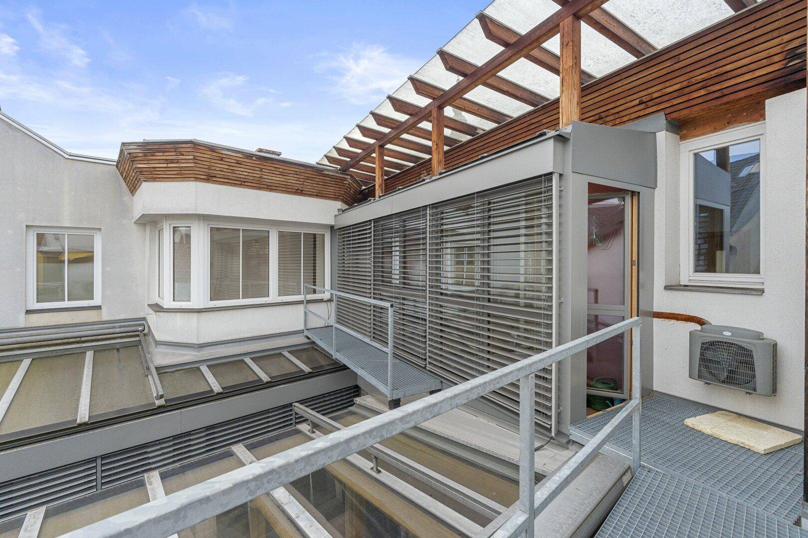 Außenansicht eines Gebäudes mit modernen Fensterfronten, Holzverkleidung und einer überdachten Terrasse.