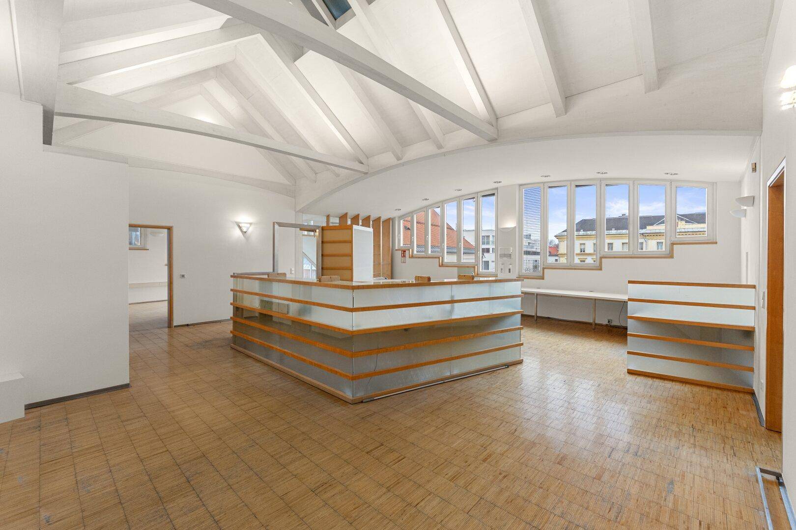 Großzügiger Bürobereich mit Holzbalken, Dachfenstern und einer modernen Empfangstheke, ideal für offene Arbeitskonzepte.