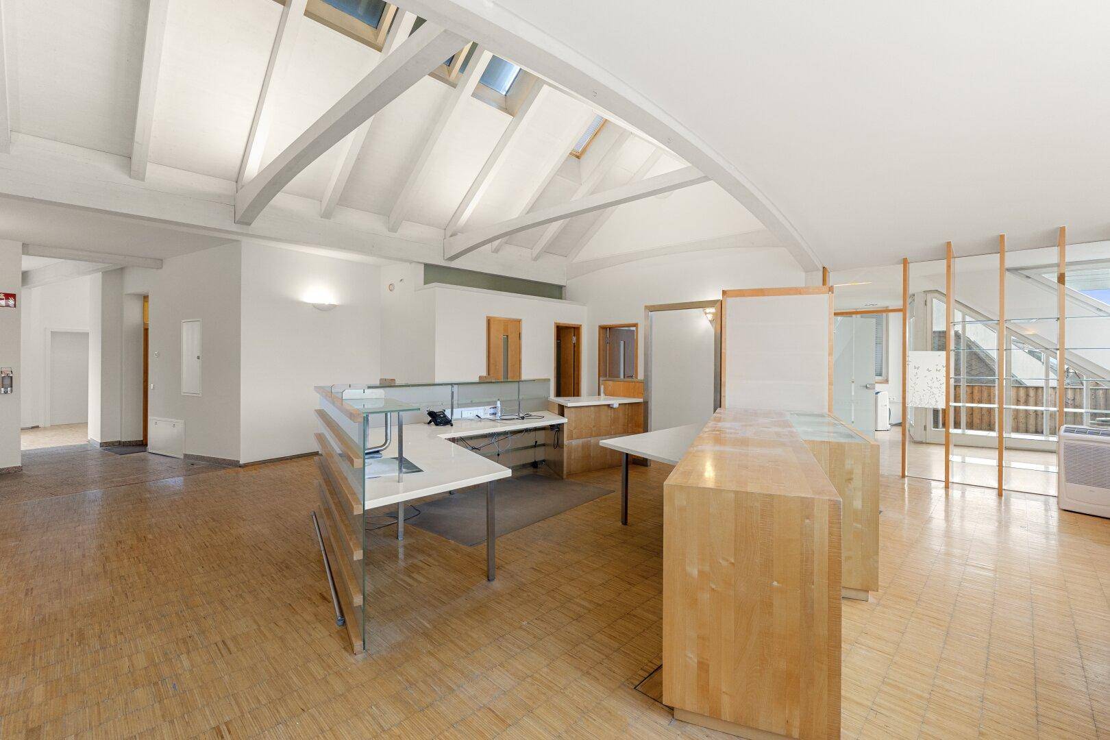 Offener Büroraum mit Holzbalken, Dachfenstern und modernen Arbeitsplätzen, bietet eine helle Arbeitsumgebung.