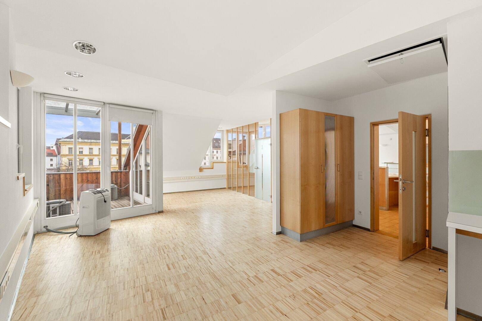 Heller Büroraum mit Holzboden, Zugang zu einem Balkon und eingebauten Schränken, bietet eine angenehme Arbeitsatmosphäre.
