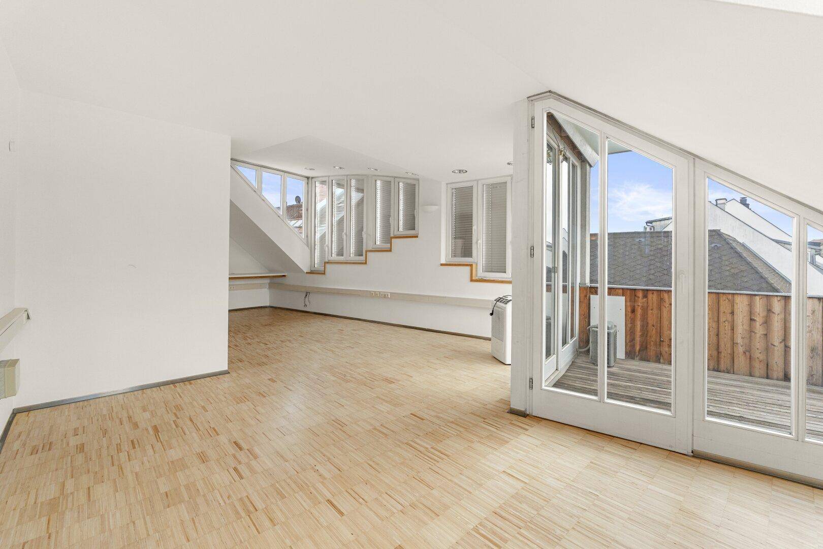 Geräumiger Büroraum mit Holzboden, großen Fenstern und Zugang zu einer Terrasse, bietet viel Tageslicht.