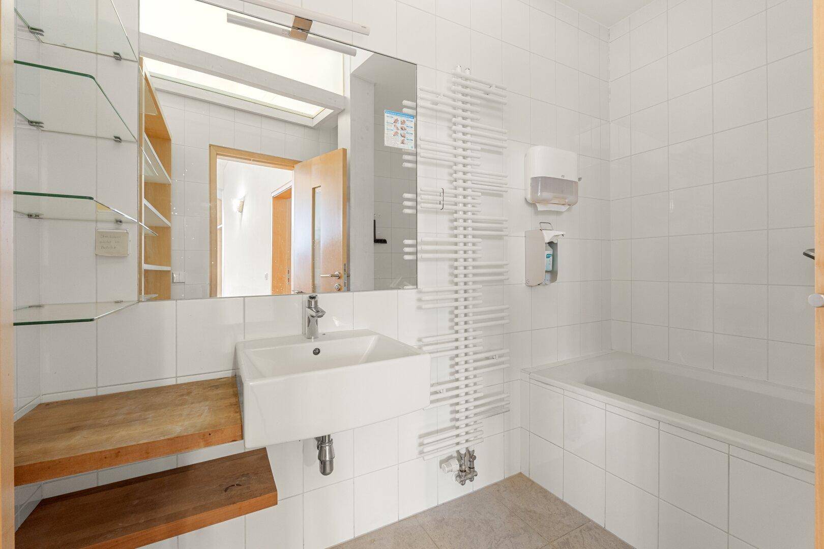 Modernes Badezimmer mit weißen Fliesen, Badewanne, Waschbecken und Handtuchheizkörper, bietet viel Licht.