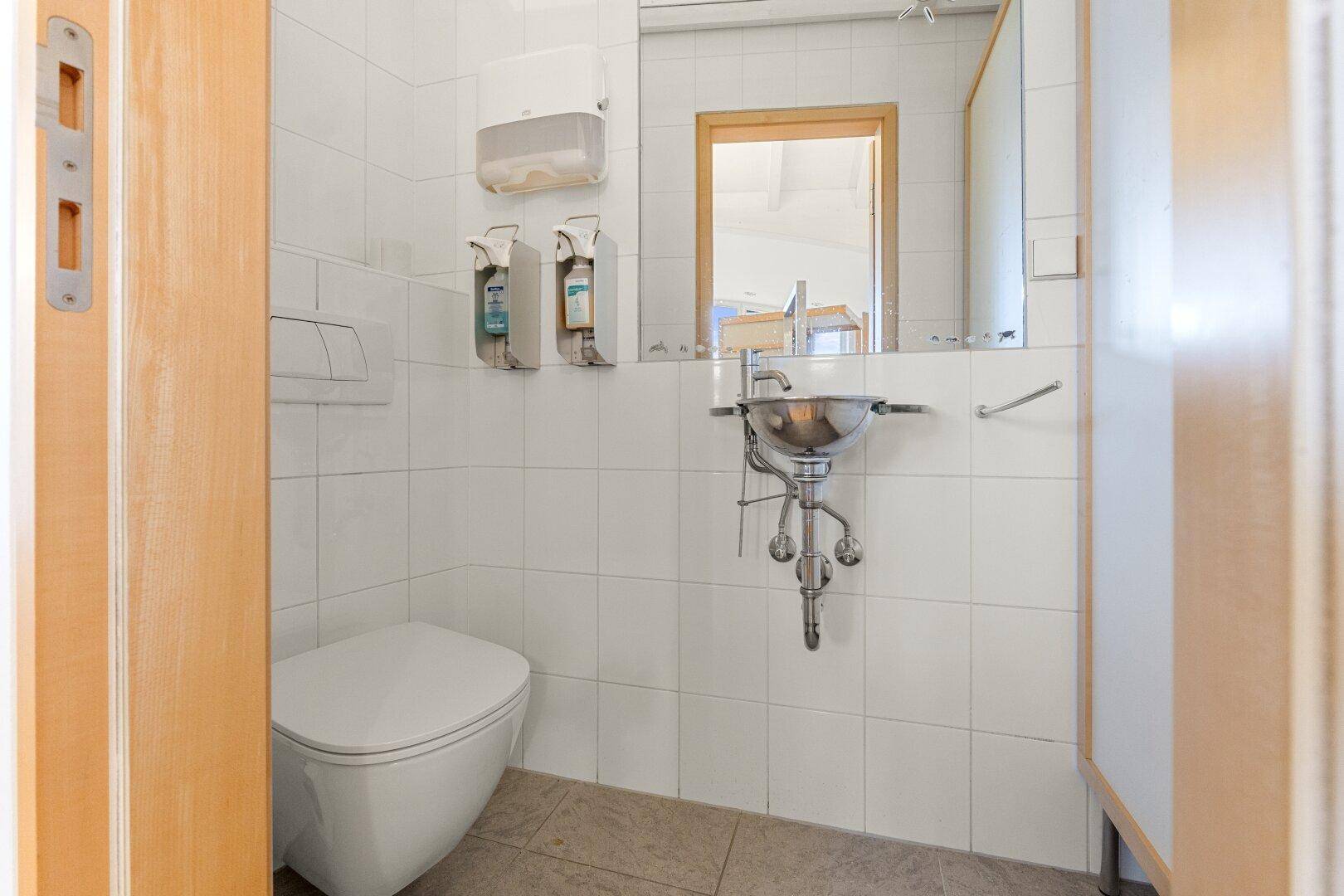 Kleines Gäste-WC mit weißen Fliesen, wandhängender Toilette und kleinem Waschbecken, funktional und sauber.