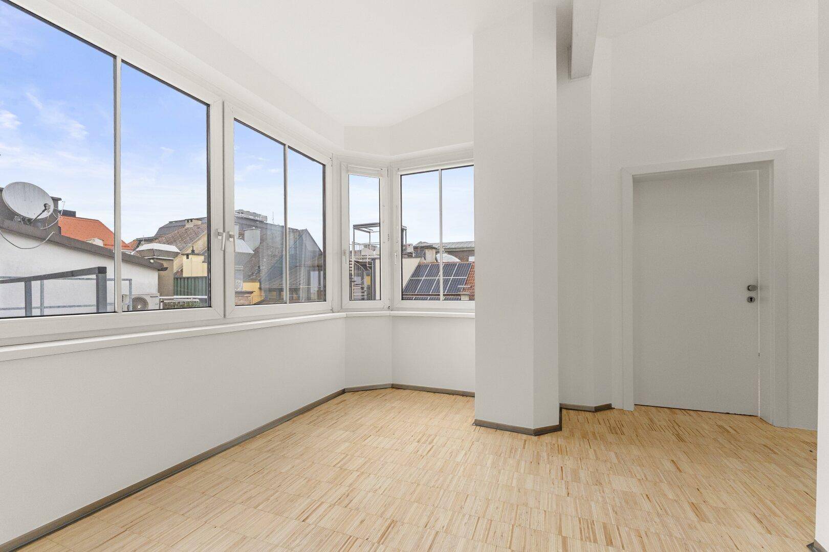 Heller Büroraum mit Holzboden und großen Fenstern, die einen weiten Blick über die Stadt bieten.