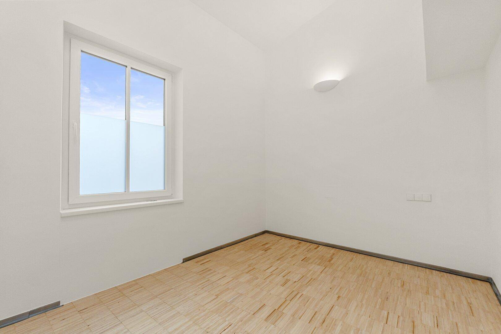 Kleiner, heller Büroraum mit Holzboden und einem Fenster, das für natürliches Licht sorgt.