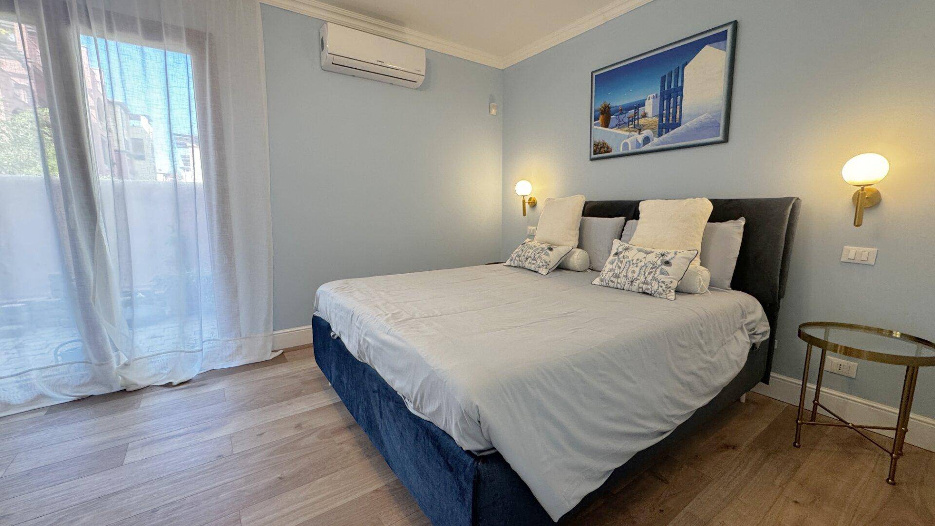 Helles Schlafzimmer mit Doppelbett, Holzboden und Zugang zu einem Balkon.