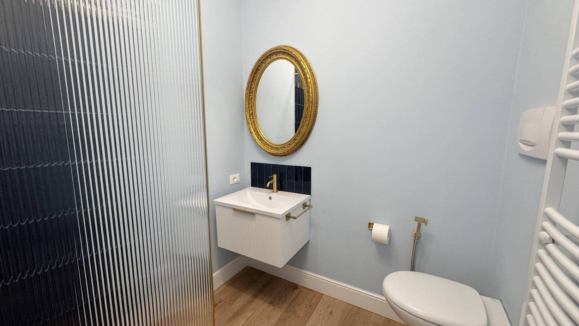 Badezimmer mit modernem Waschtisch, goldenem Spiegel und Duschbereich.