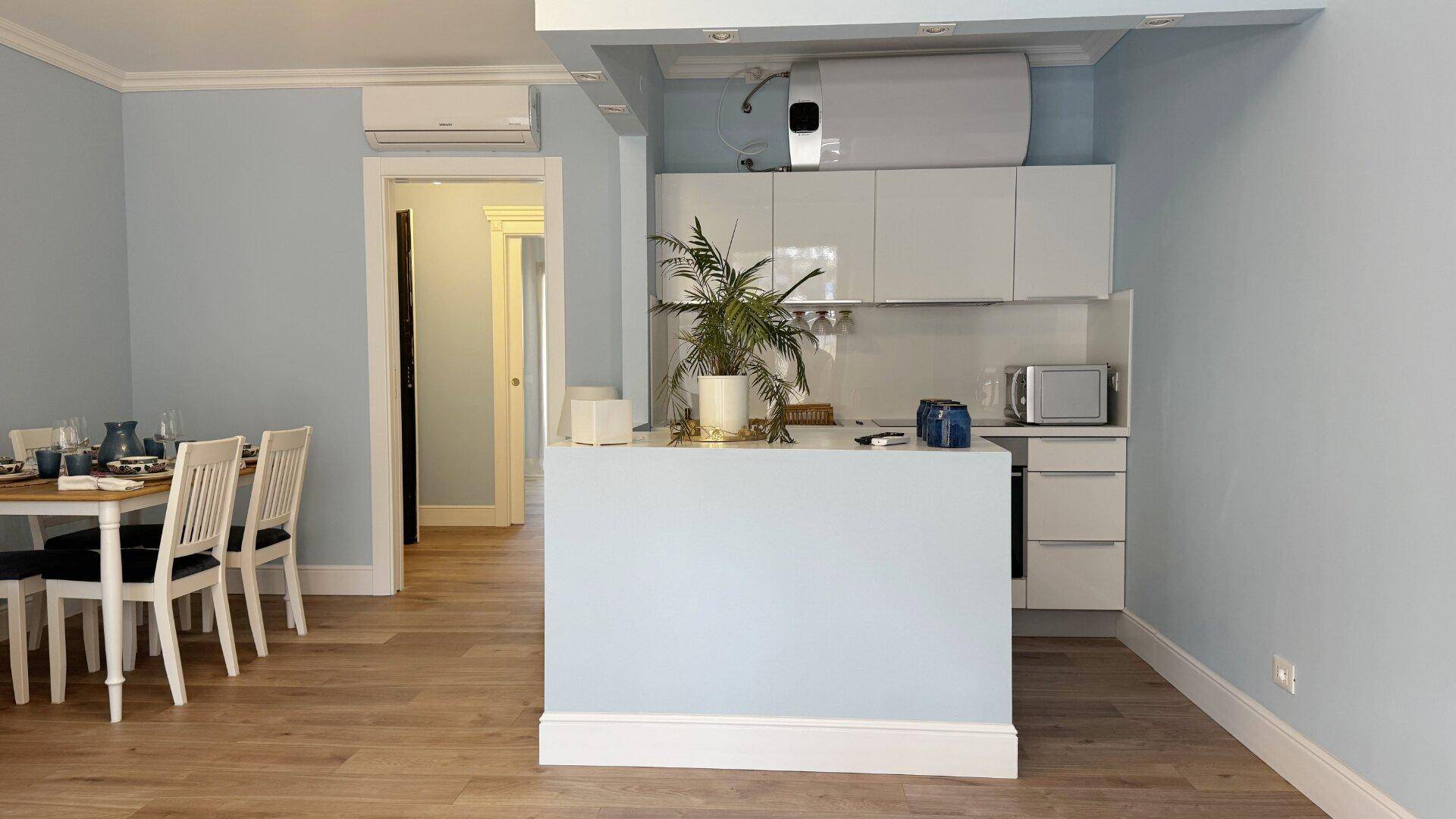 Moderne offene Küche mit weißen Schränken und Essbereich in einem hellen Wohnraum.