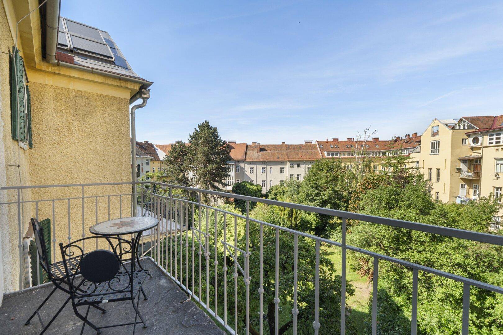 Kleiner Balkon mit Sitzgelegenheiten, Blick auf einen grünen Innenhof und umliegende Gebäude.