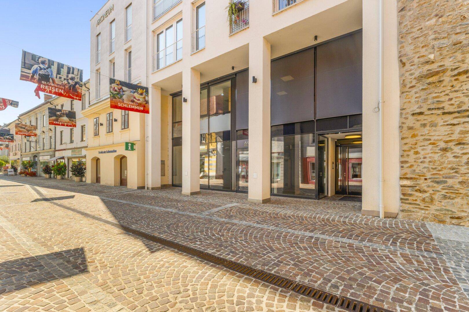 Moderne Gebäudefassade mit großen Glasfronten und Eingangsbereich an einer belebten Straße.