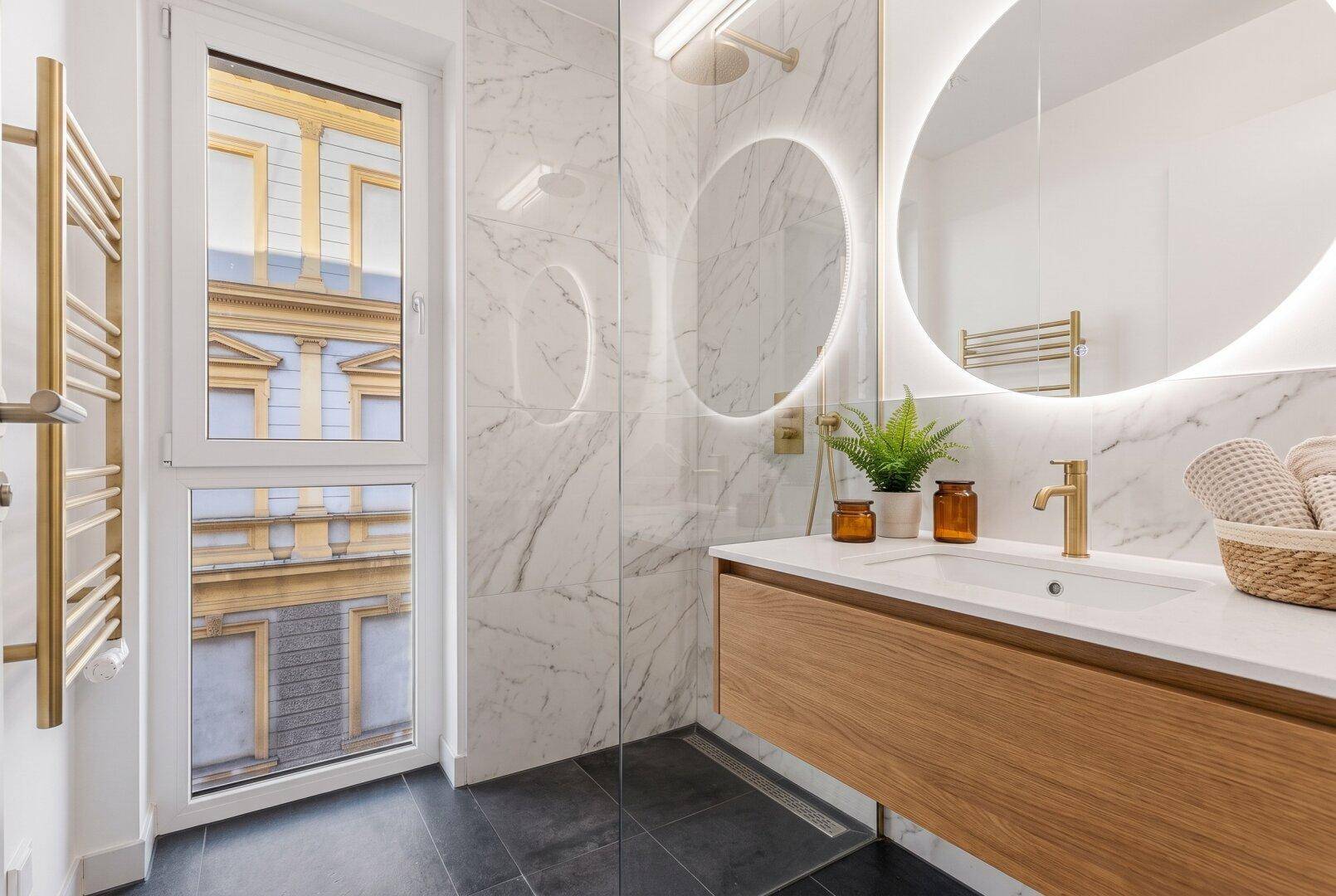 Modernes Badezimmer mit Marmorfliesen, beleuchtetem Spiegel und Dusche.