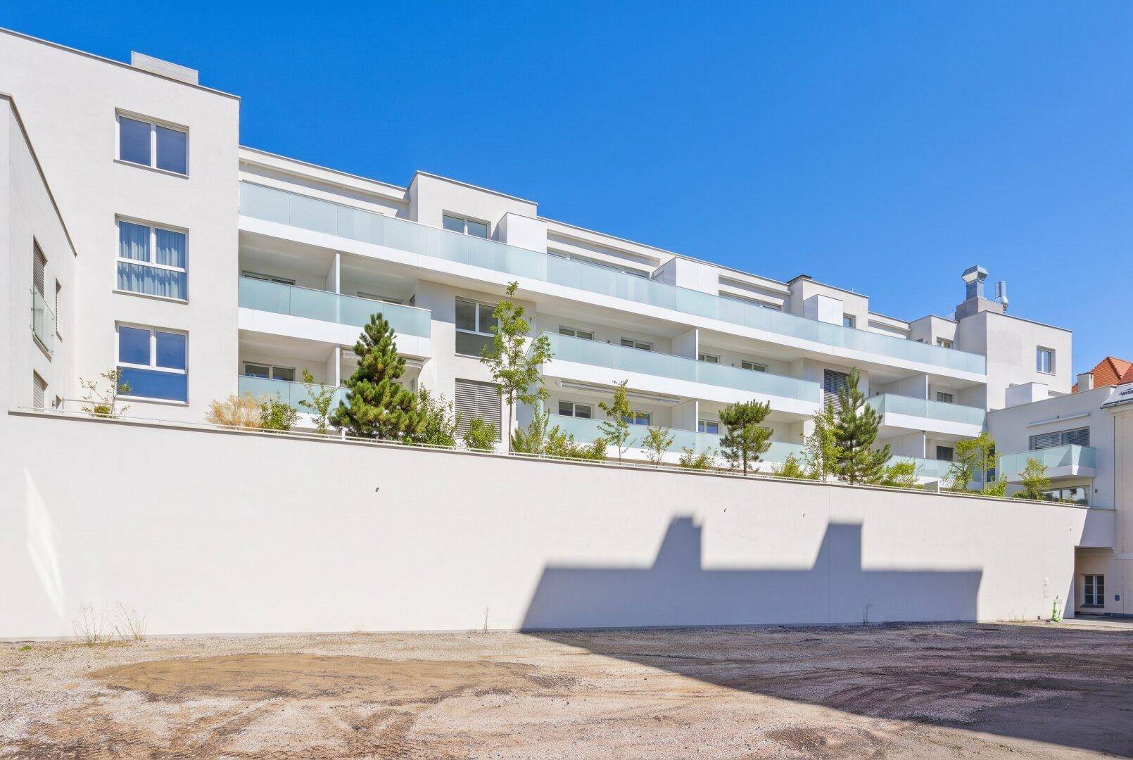 Moderne Wohnanlage mit weißer Fassade und Balkonen unter blauem Himmel.