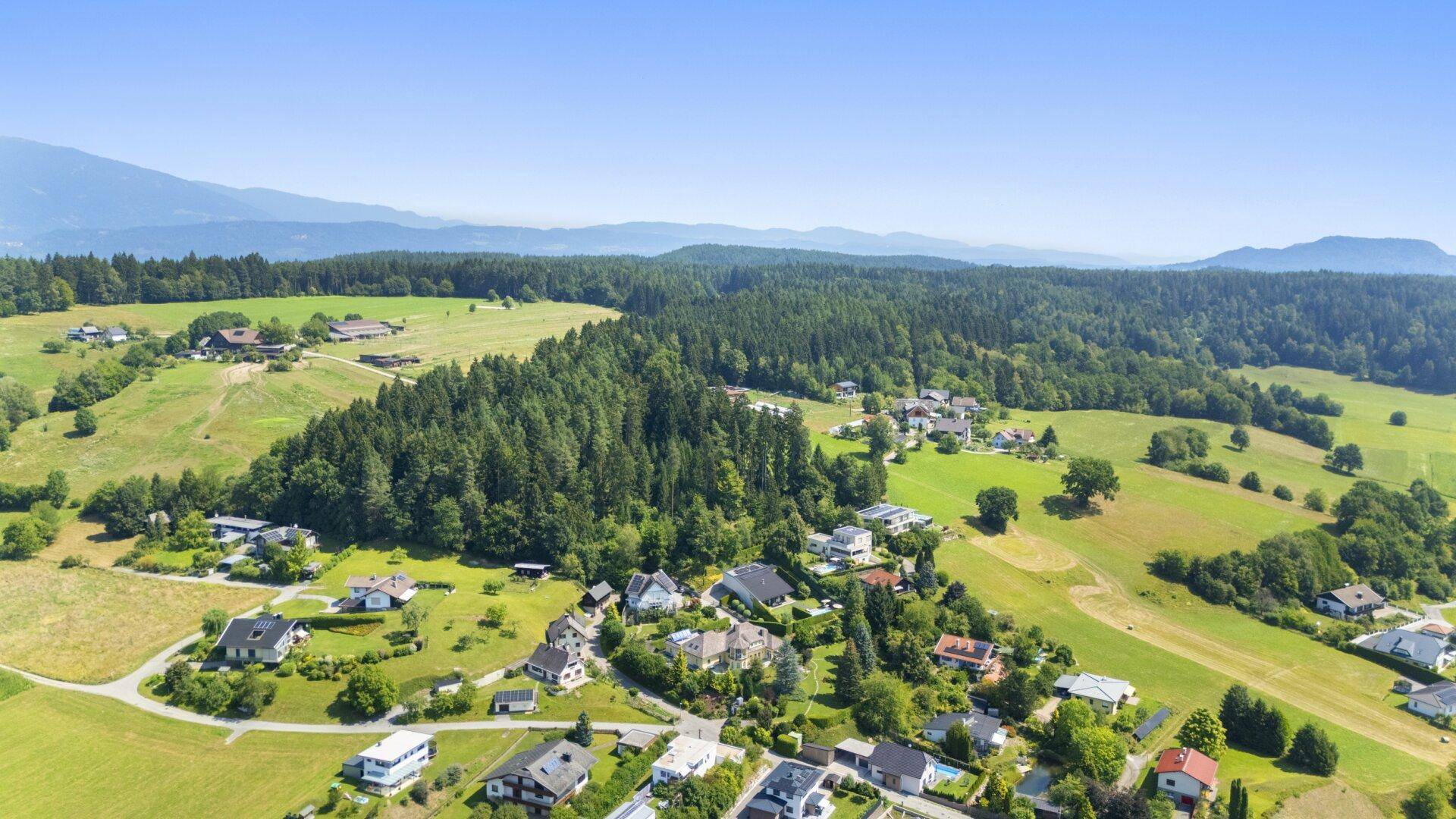 Panoramablick auf eine idyllische Landschaft mit verstreuten Häusern, Feldern und dichten Wäldern.