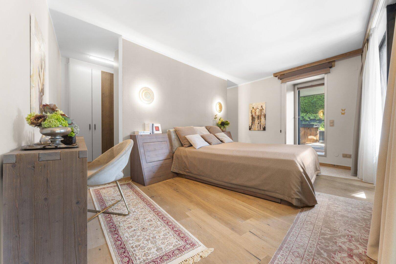 Helles Schlafzimmer mit Holzboden, großem Bett und Zugang zum Außenbereich.