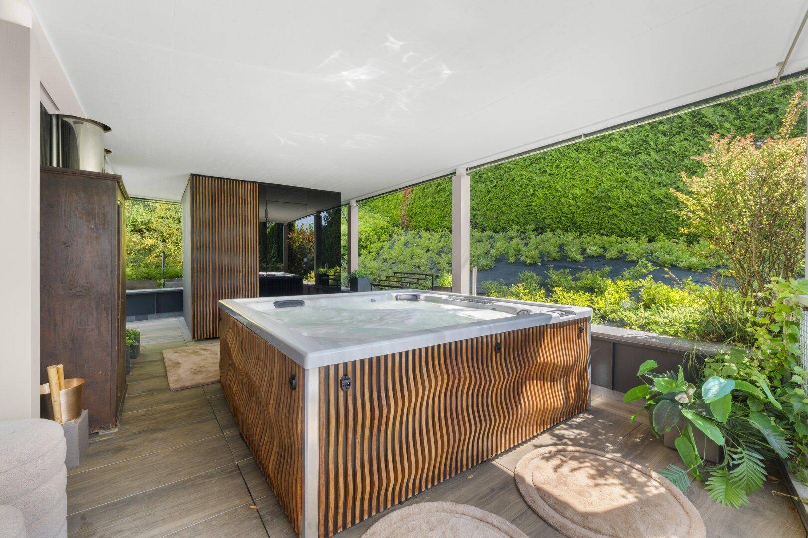Luxuriöser Whirlpool auf der Terrasse, umgeben von grüner Bepflanzung.