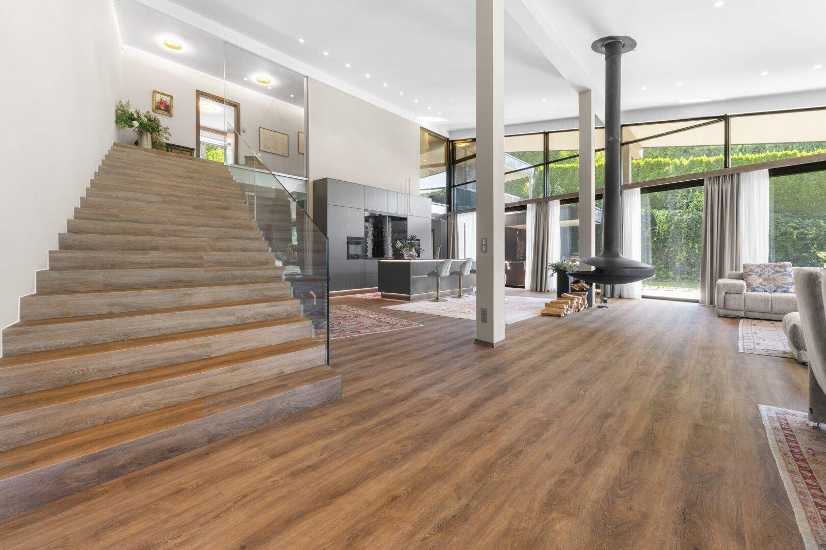 Moderner Wohnbereich mit offener Küche, Holztreppe und raumhohen Fenstern.