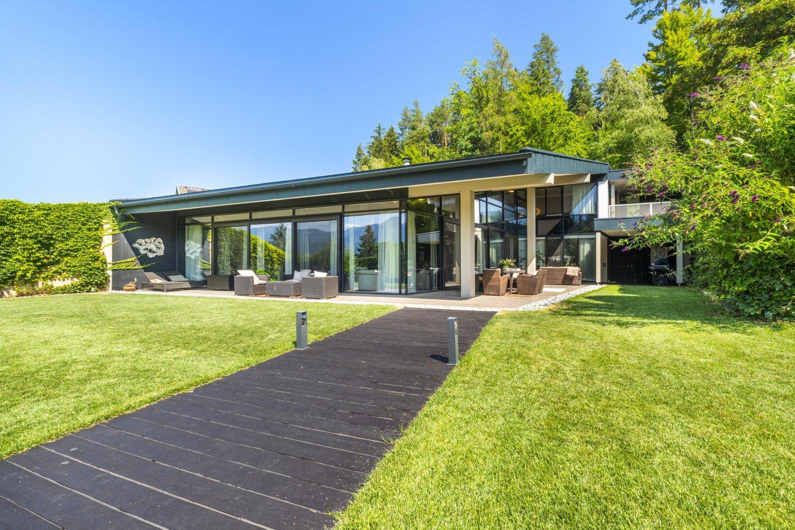 Moderne Villa mit weitläufigem Garten, Holzsteg und üppiger Bepflanzung.