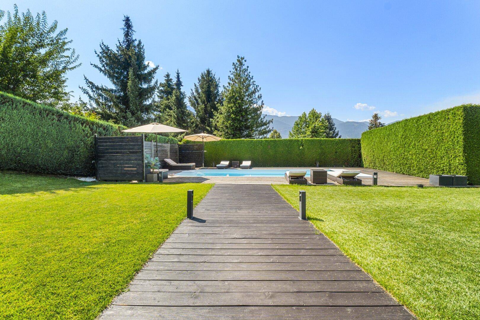 Weitläufiger Gartenbereich mit Pool, Holzdeck und hohen Hecken für Privatsphäre.