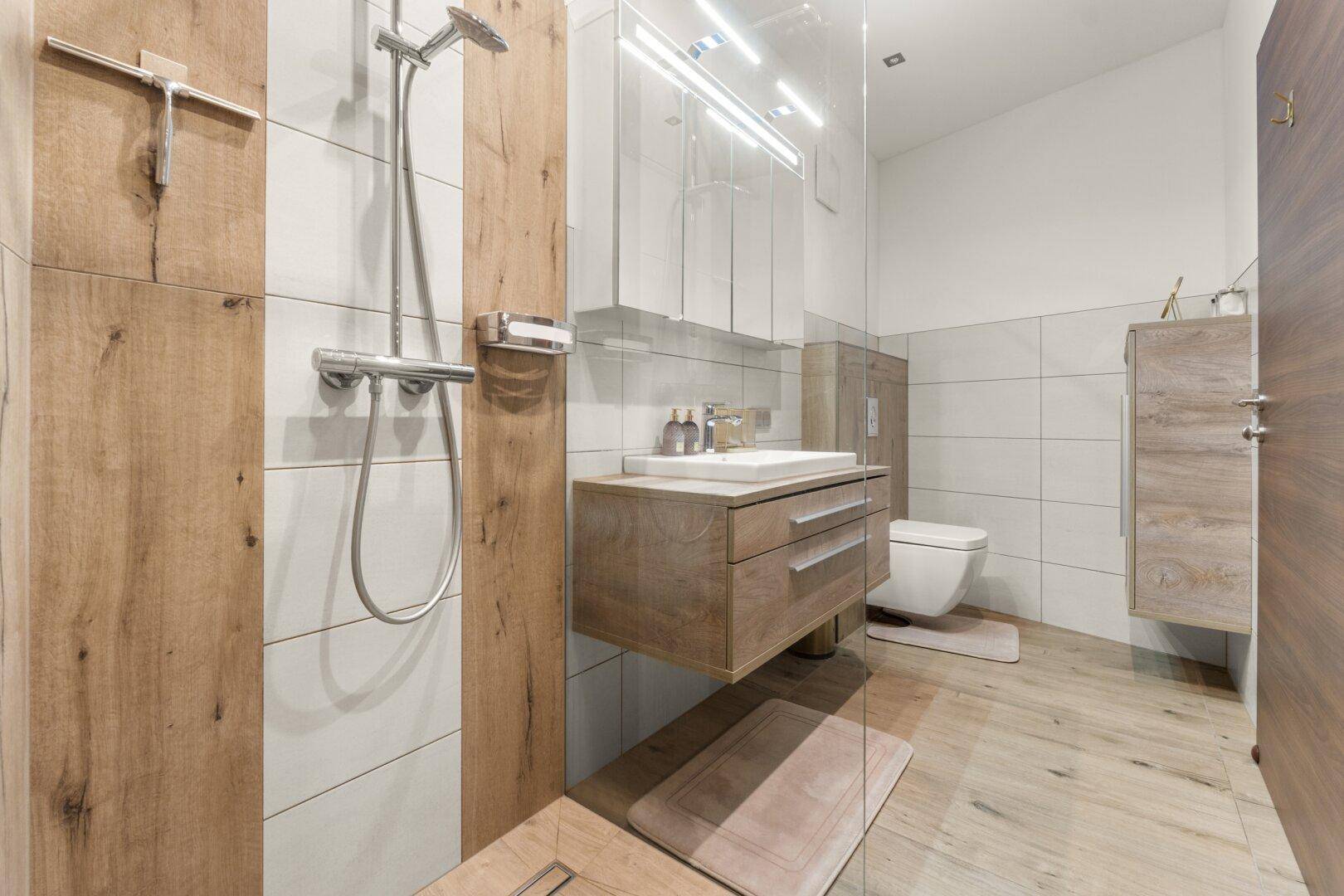 Modernes Badezimmer mit begehbarer Dusche, schwebendem Waschtisch und Holzelementen.