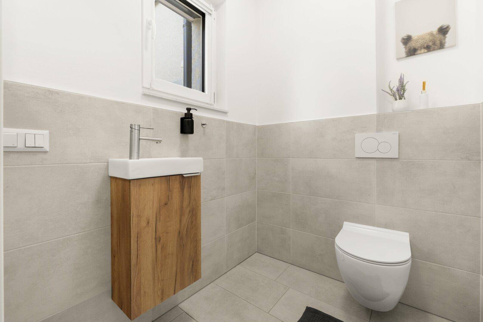 Modernes Gäste-WC mit wandhängendem WC, kleinem Waschbecken und Fenster.