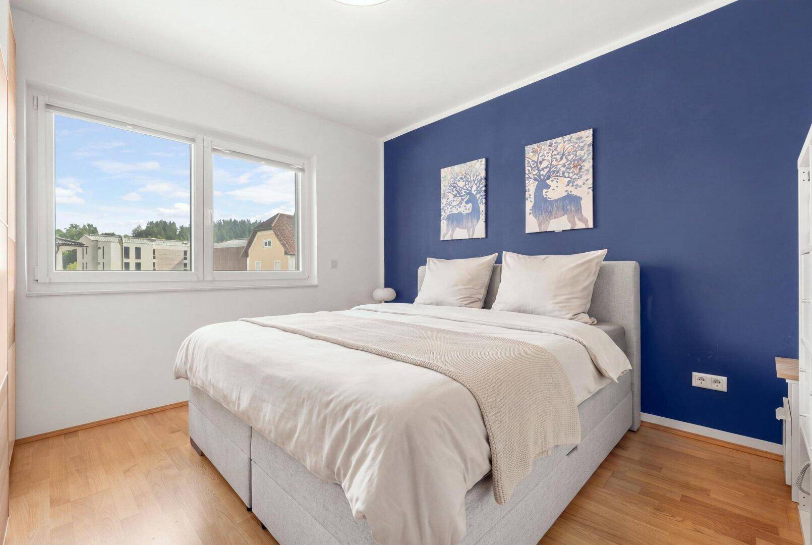 Schlafzimmer mit Doppelbett, blauer Akzentwand und hellem Holzboden.