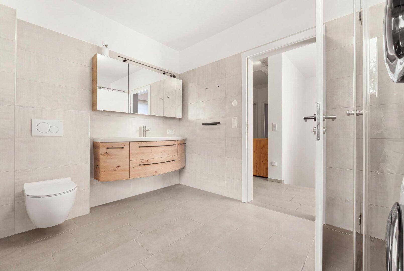 Modernes Badezimmer mit Holzwaschtisch, wandhängendem WC und Spiegelschrank.
