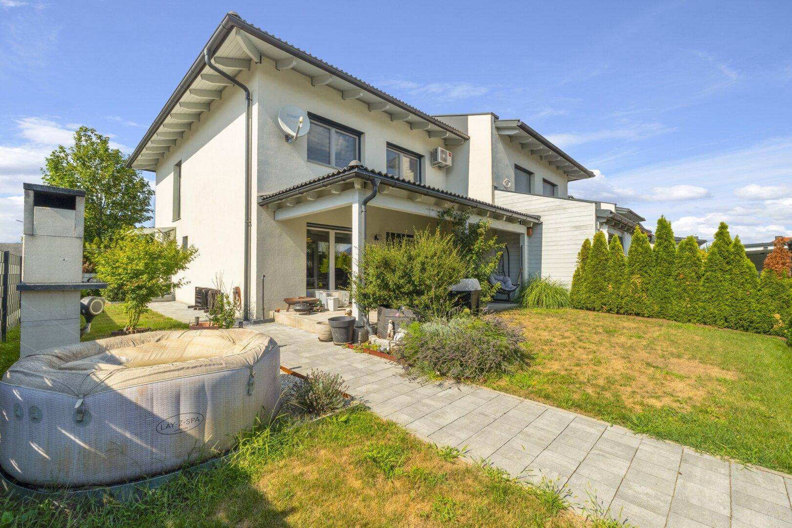 Garten mit Rasenfläche, Terrasse, Grillplatz und aufblasbarem Whirlpool.