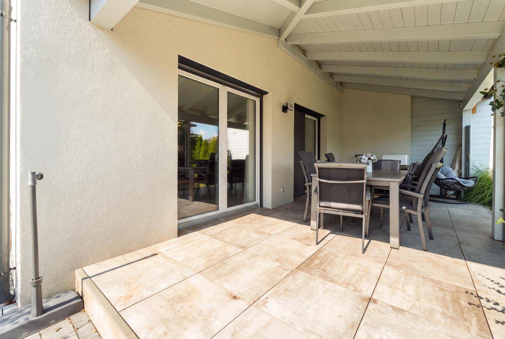 Überdachte Terrasse mit modernen Gartenmöbeln und Zugang zum Wohnbereich.