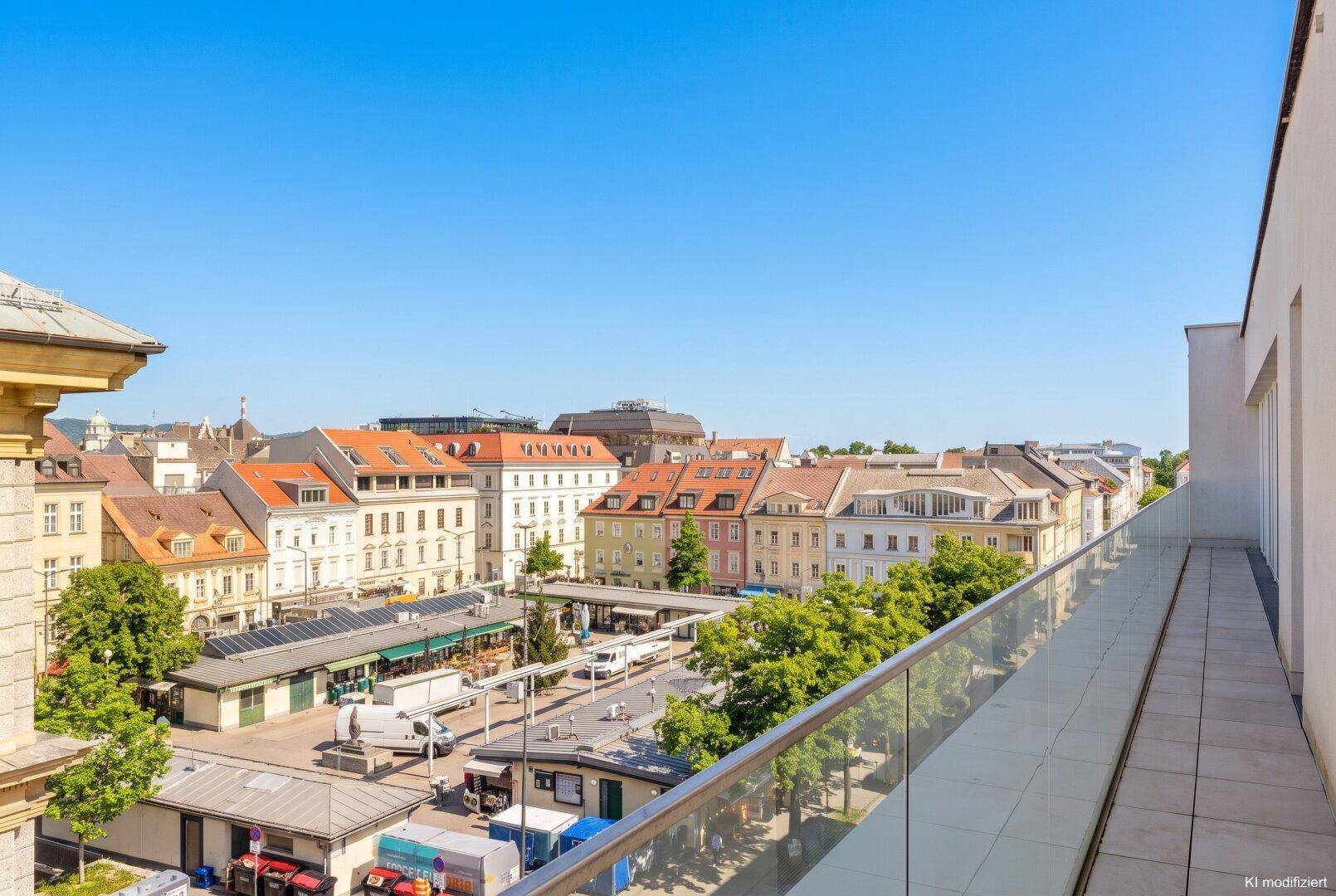 Weitläufige Terrasse mit Glasgeländer bietet einen Panoramablick über den belebten Stadtplatz.
