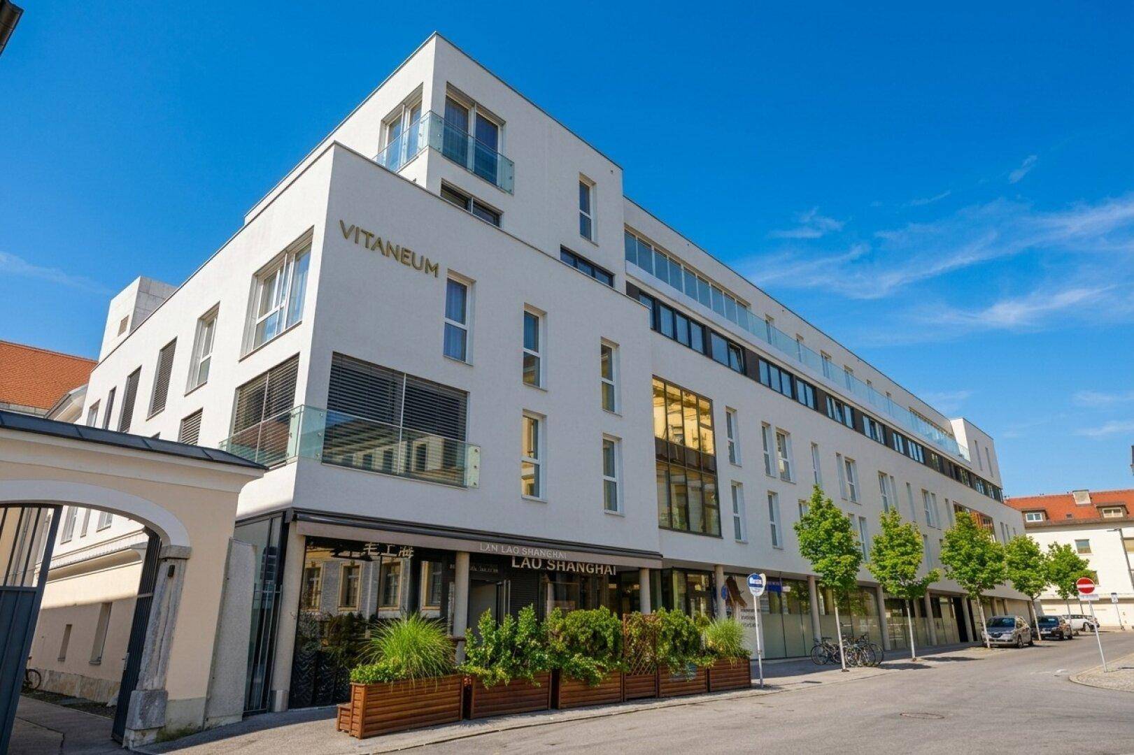 Modernes weißes Gebäude mit klaren Linien, großen Fenstern und Geschäften im Erdgeschoss.
