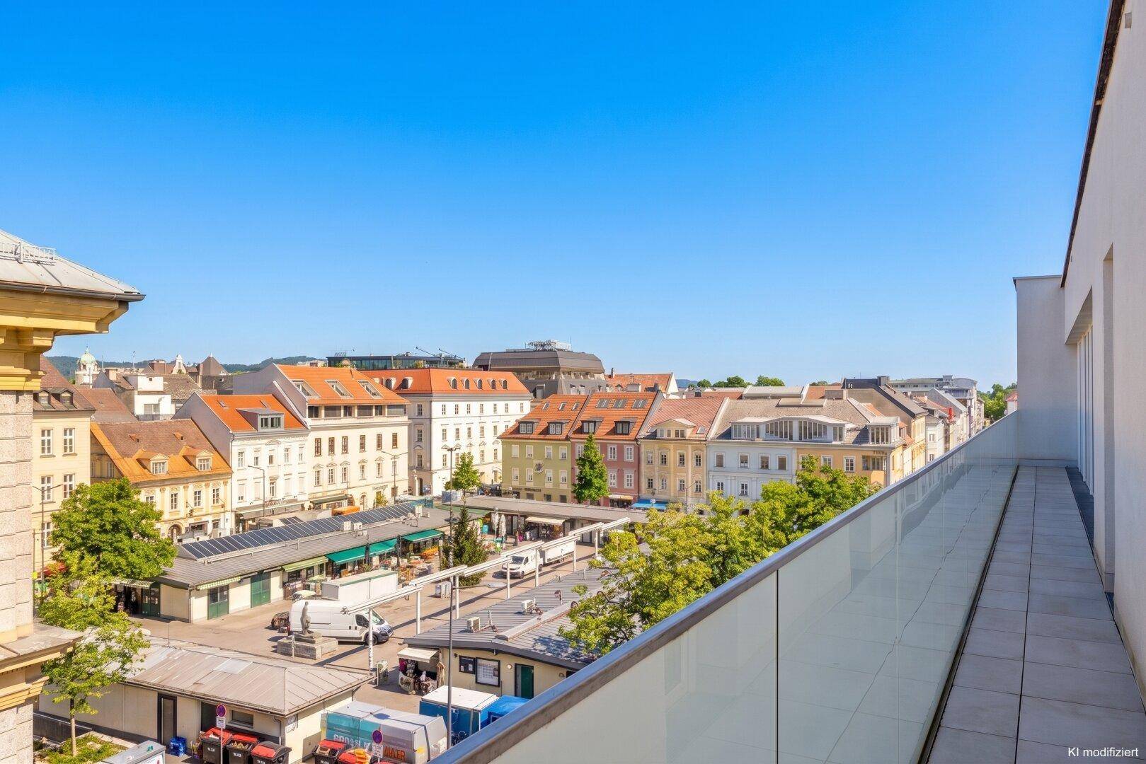 Lange Terrasse mit weitem Blick über einen belebten Stadtplatz und historische Gebäude.