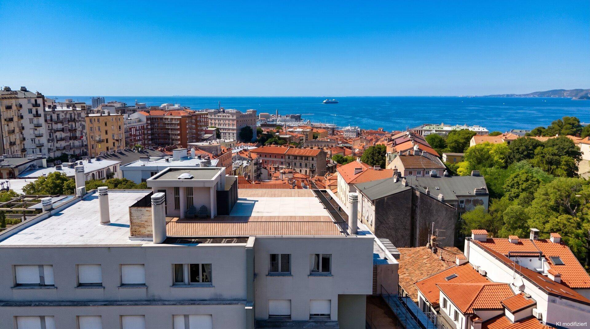 Panoramablick über die Stadt mit roten Dächern und dem weiten blauen Meer im Hintergrund.