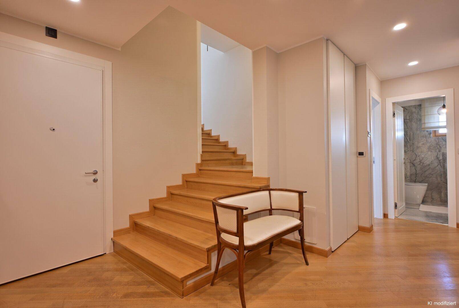 Heller Eingangsbereich mit Holztreppe und Parkettboden, der zu den oberen Etagen führt.