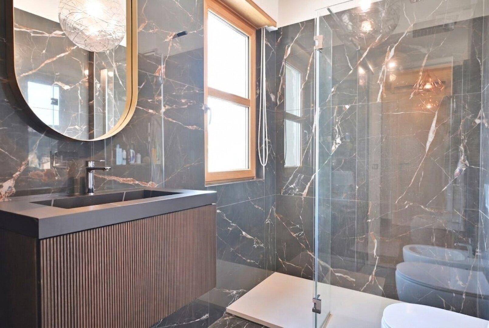 Elegantes Badezimmer mit dunklen Marmorfliesen, begehbarer Dusche und modernem Waschtisch.