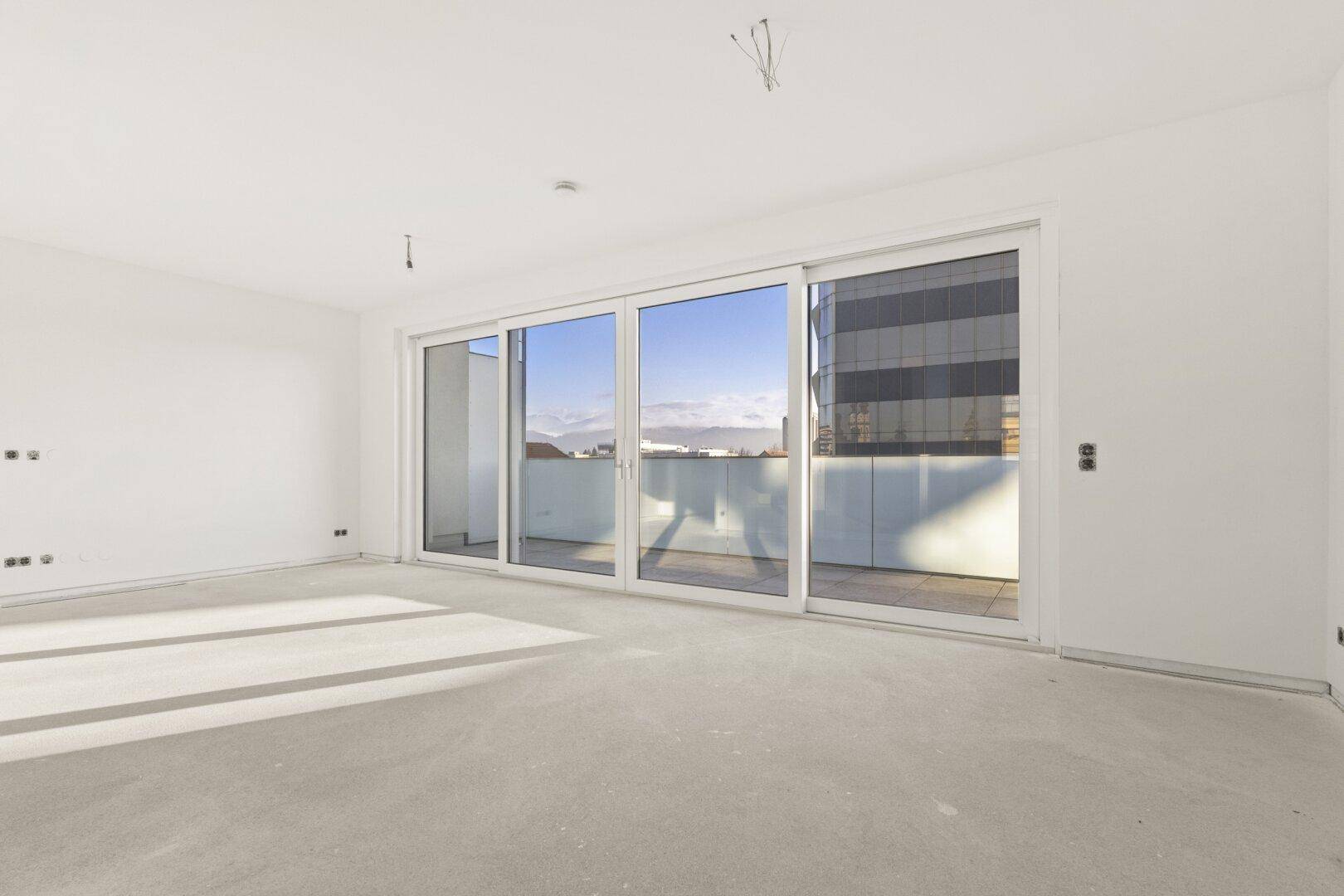 Geräumiger Wohnbereich mit breiter Fensterfront und Blick auf die städtische Umgebung, ideal für modernes Wohnen.