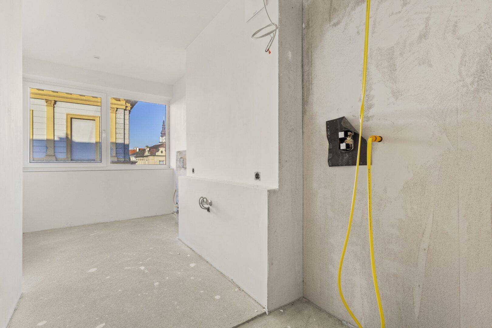 Unfertiges Badezimmer im Rohbau mit Fenster und sichtbaren Installationen, bereit für den Ausbau.