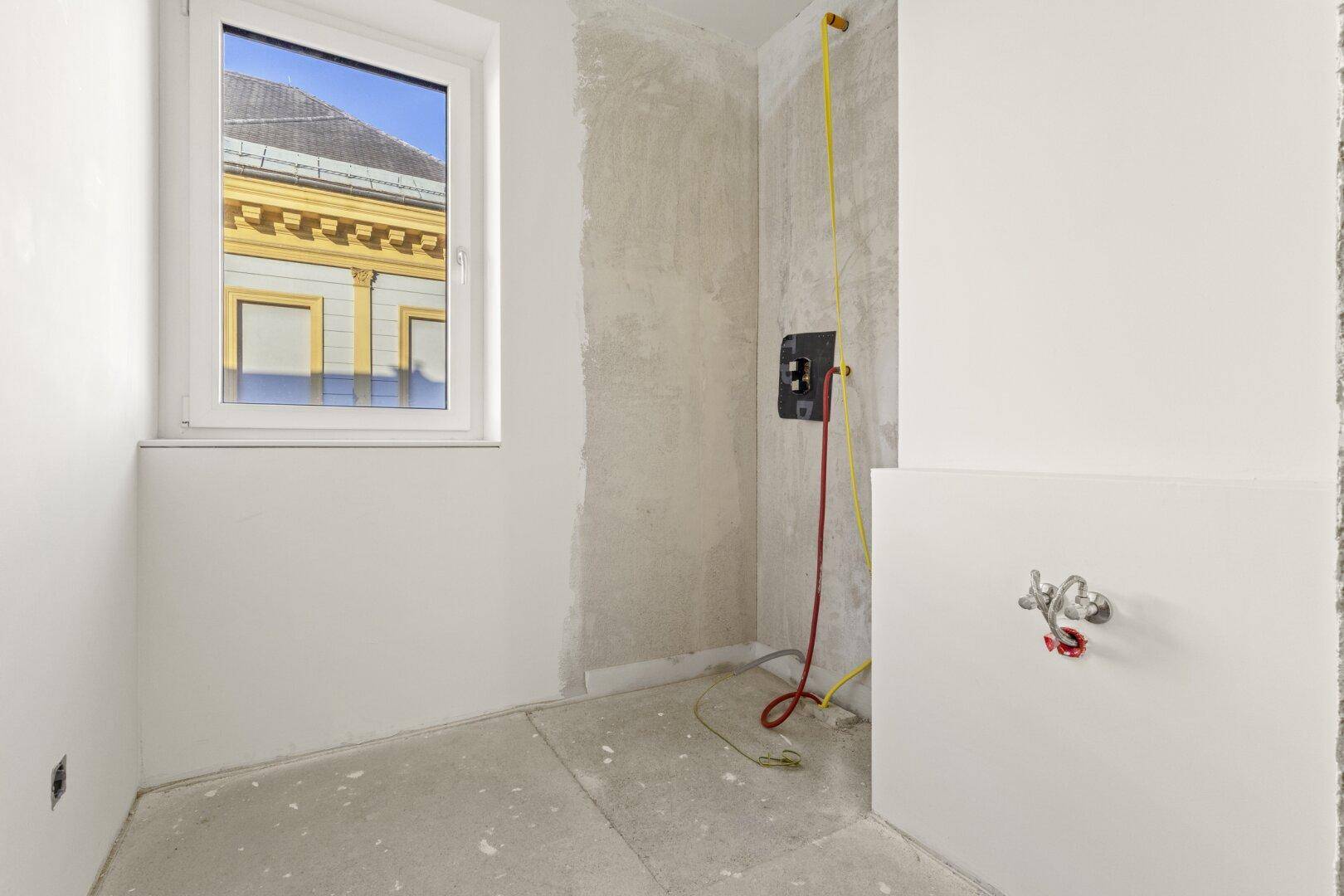 Badezimmer im Rohbau mit Fenster und vorbereiteten Anschlüssen, bereit für die Endmontage der Sanitärobjekte.