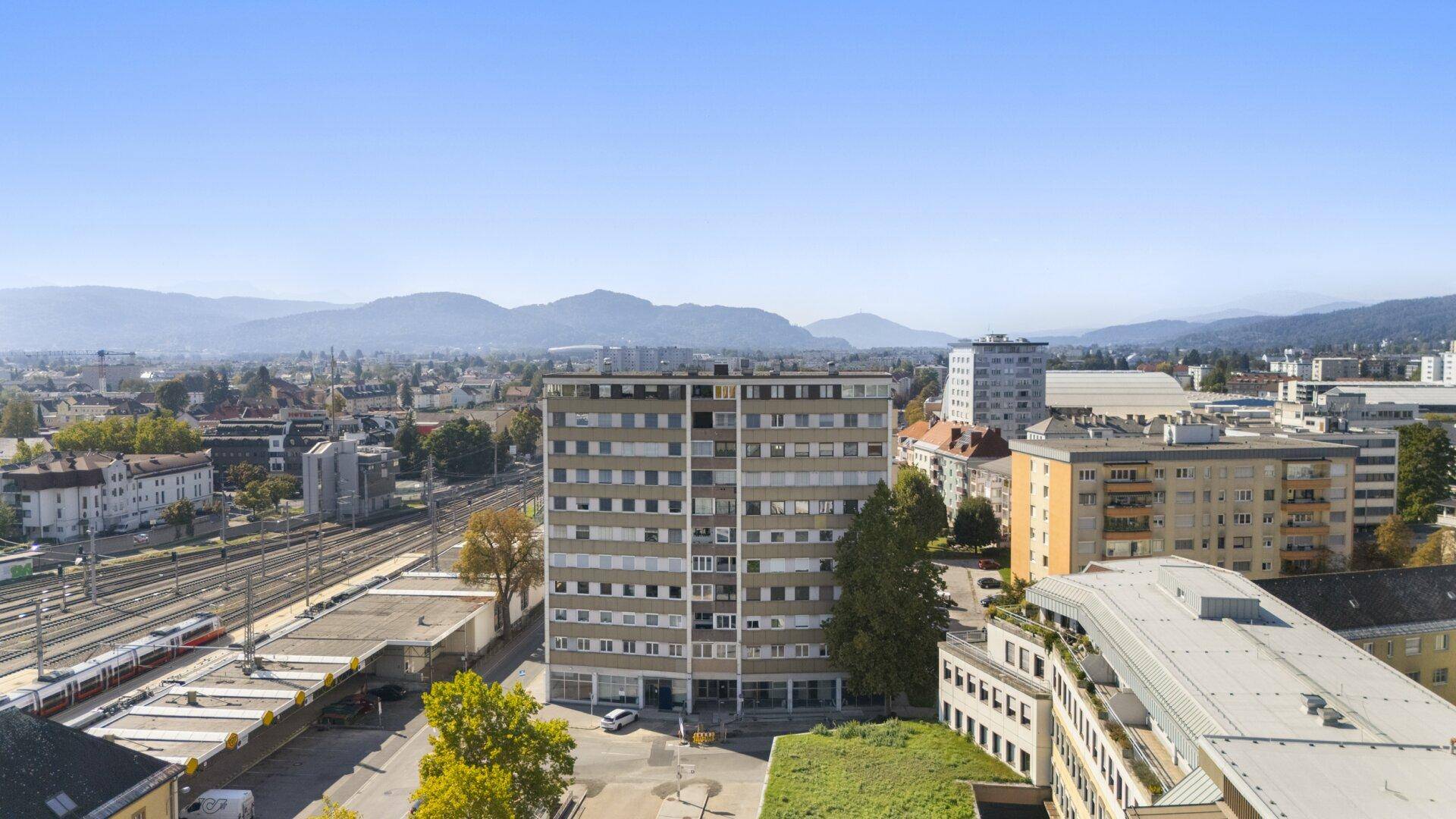 Weitläufige Ansicht des Wohnkomplexes mit Bahnanlagen und Bergpanorama im Hintergrund.