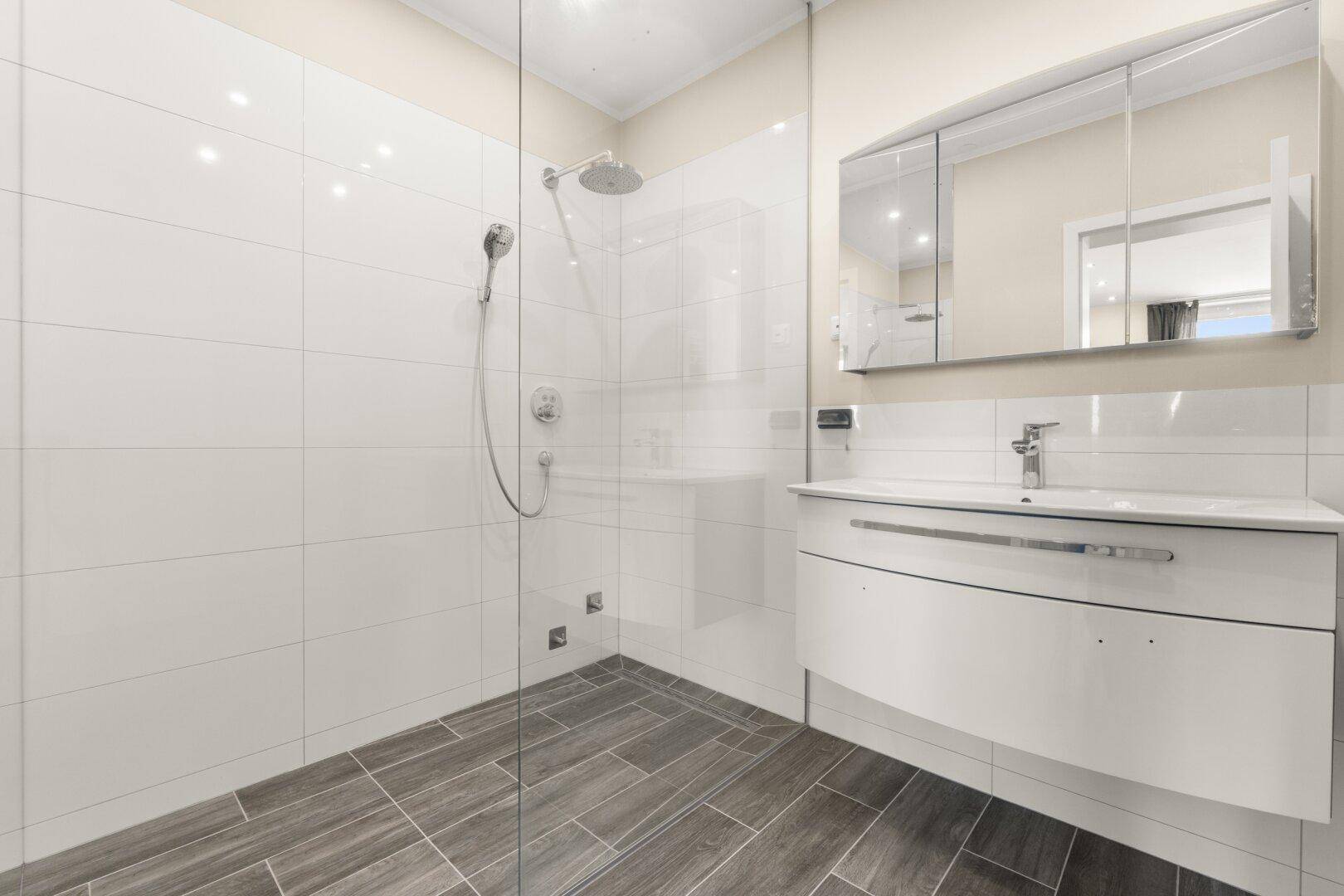 Modernes Badezimmer mit ebenerdiger Dusche, Einzelwaschbecken und Spiegelschrank.