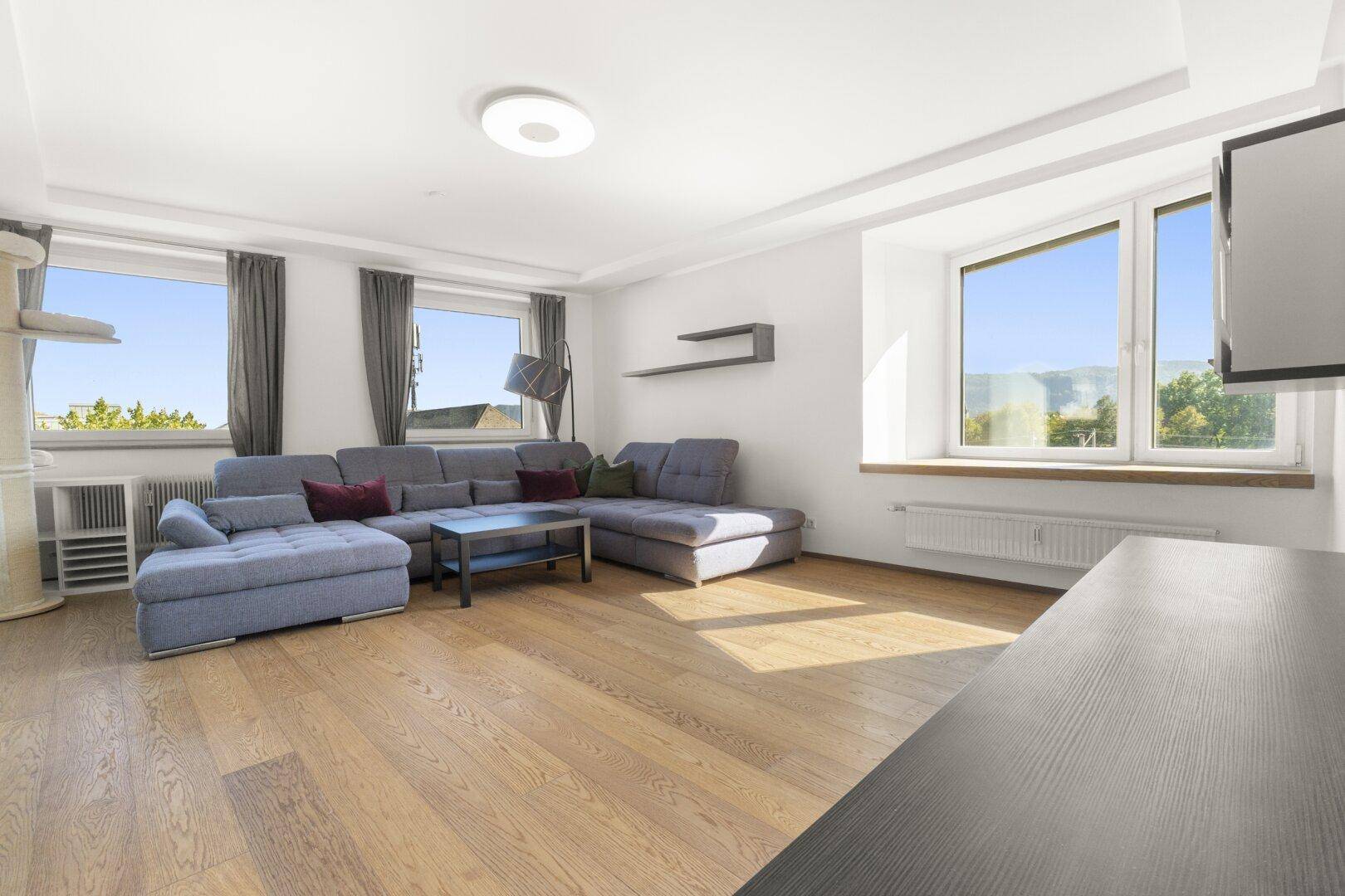 Helles Wohnzimmer mit mehreren Fenstern, Holzboden und bequemer Sitzecke.