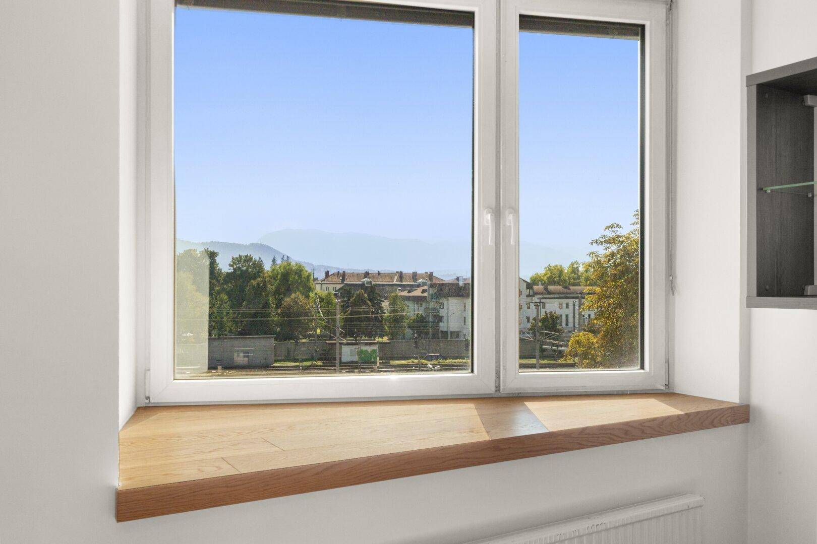 Fenster mit Holzbalken und weitem Blick über die Stadt und die Berge.