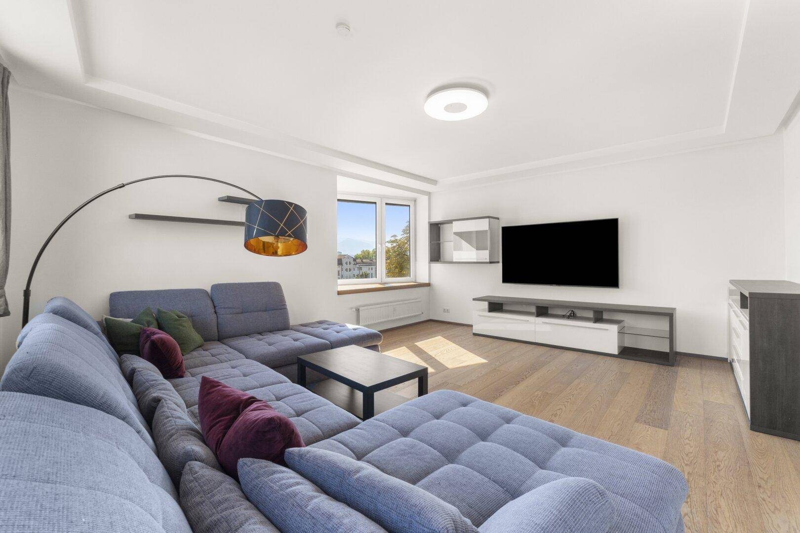 Gemütliches Wohnzimmer mit großem Ecksofa, Holzboden und modernem TV-Bereich.