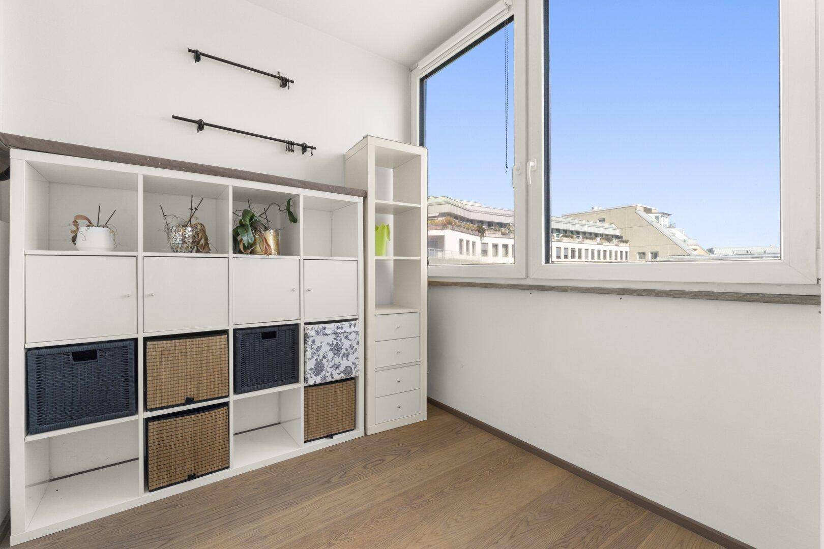 Heller Raum mit großem Fenster, Holzboden und praktischem Regalsystem.