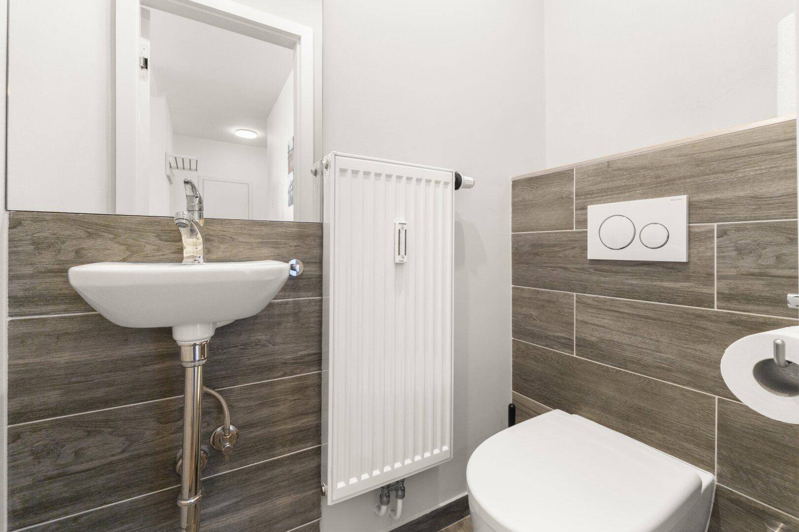 Gäste-WC mit wandhängender Toilette, kleinem Waschbecken und Heizkörper.