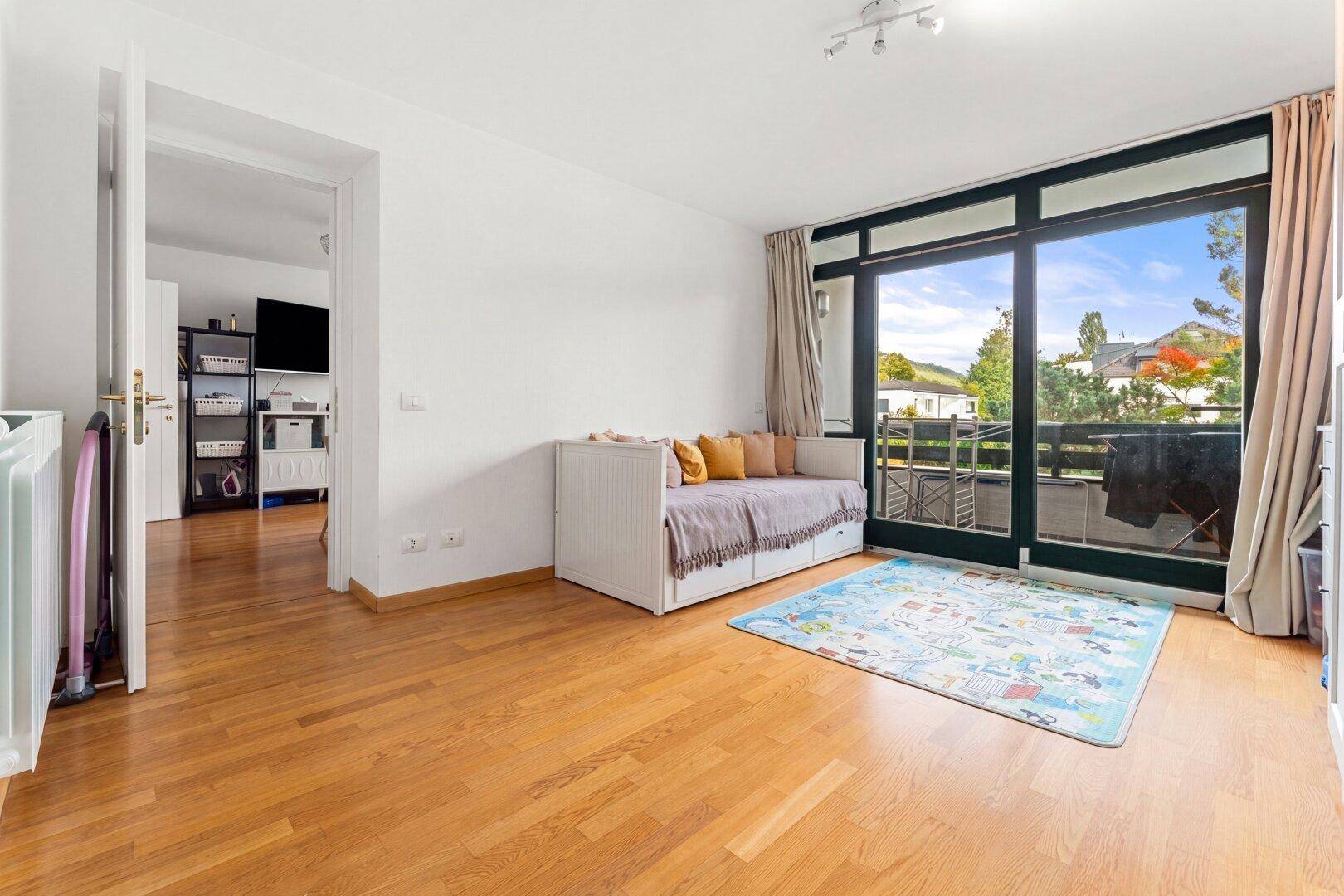 Helles Zimmer mit Holzboden und großem Fenster, das Zugang zum Balkon bietet.