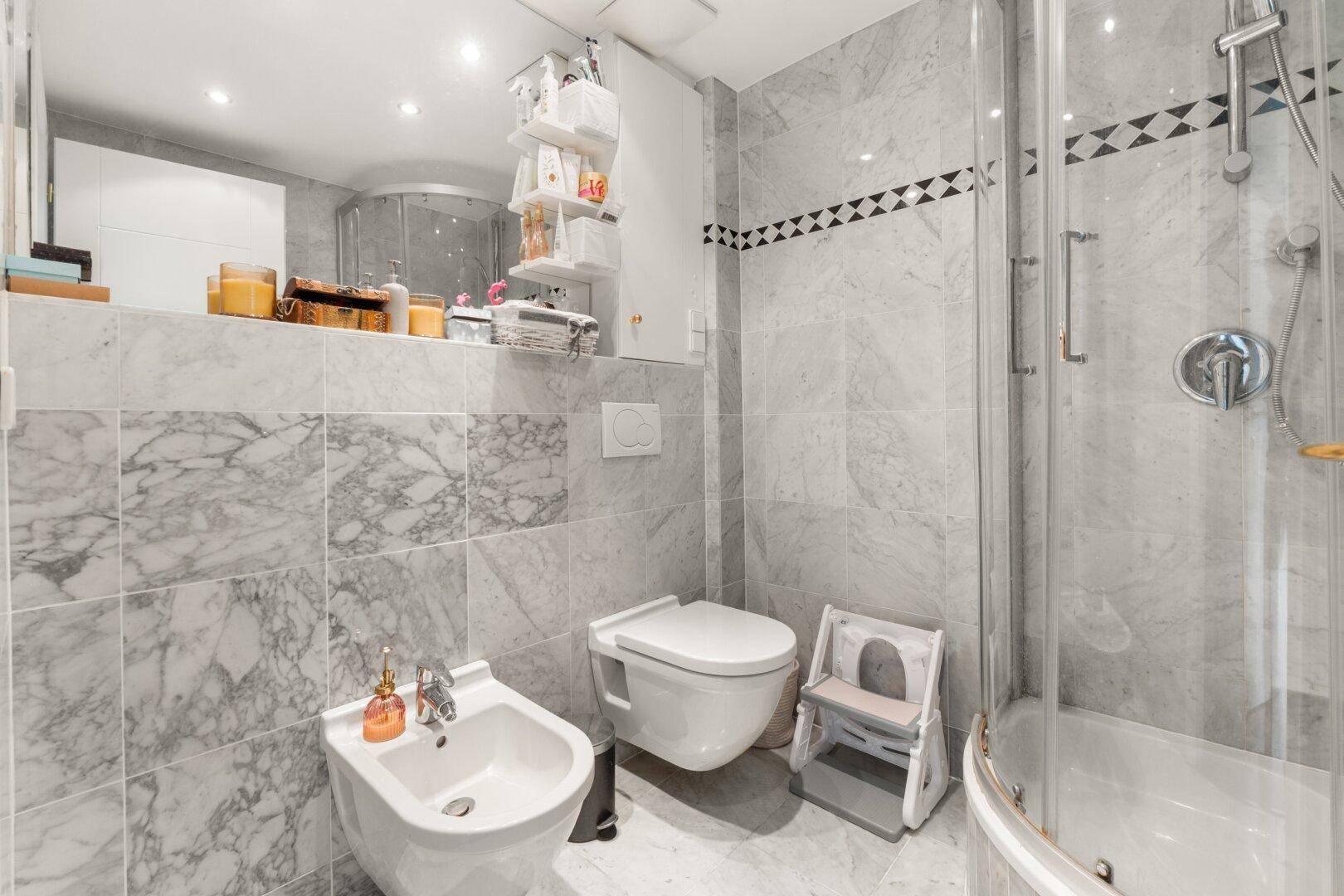 Modernes Badezimmer mit Marmorfliesen, Bidet, wandhängendem WC und Duschkabine.