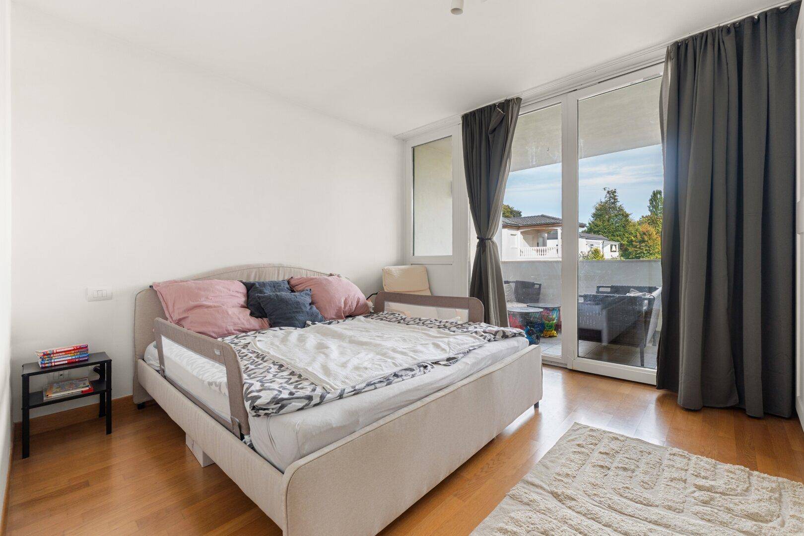 Gemütliches Schlafzimmer mit Holzboden, großem Fenster und direktem Balkonzugang.